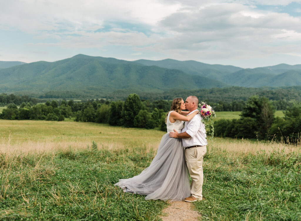 woman wearing wedding dress and holding a bouquet of flowers kissing a man with a backdrop of the Great Smoky Mountains