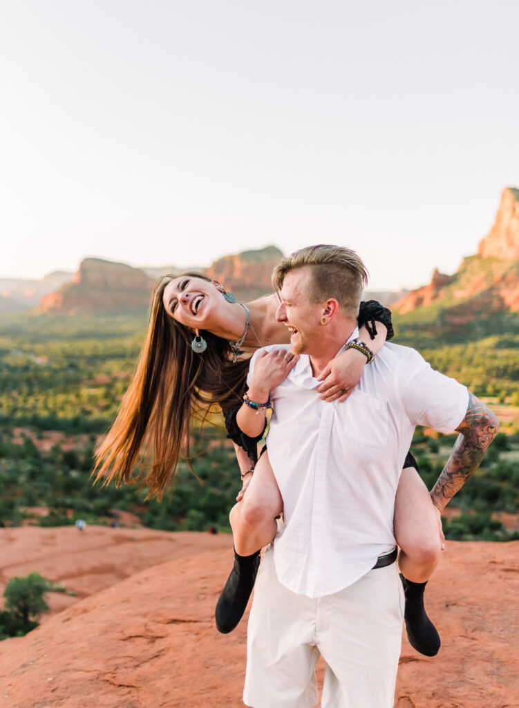 A man gives a woman a piggy back ride while on top of Bell Rock at adventure session in Sedona, Arizona
