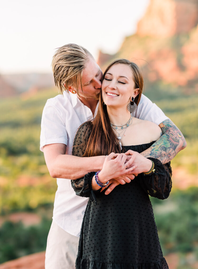 A man bear hugs a woman from behind and kisses her on the cheek in Sedona Arizona