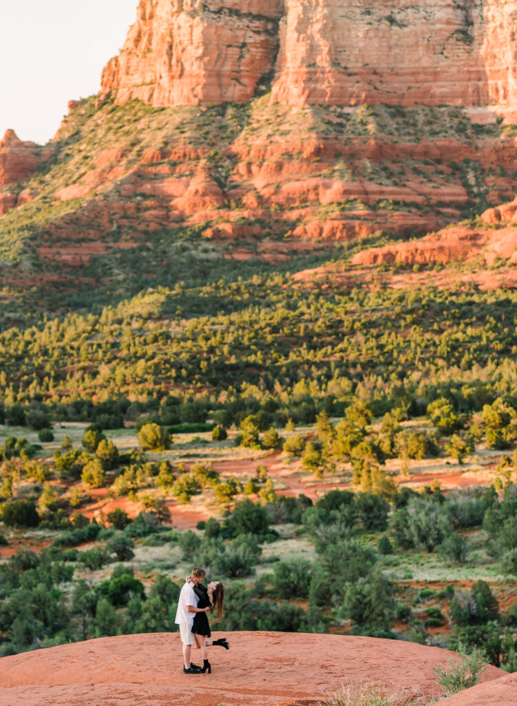 A man and a woman hug with the backdrop of the red rocks of Sedona behind them.
