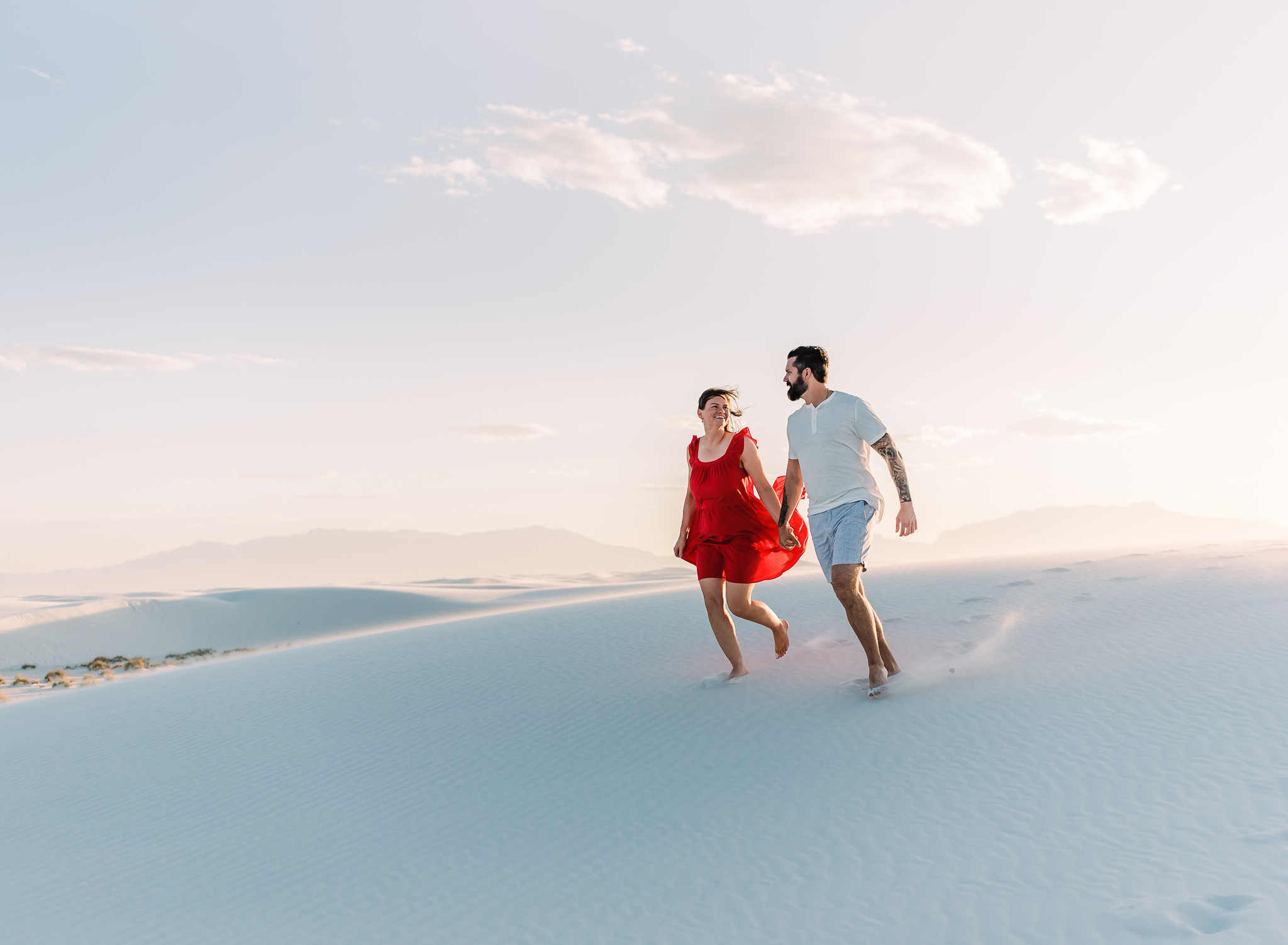 A man and woman run down a sand dune hand in hand at white sands national park