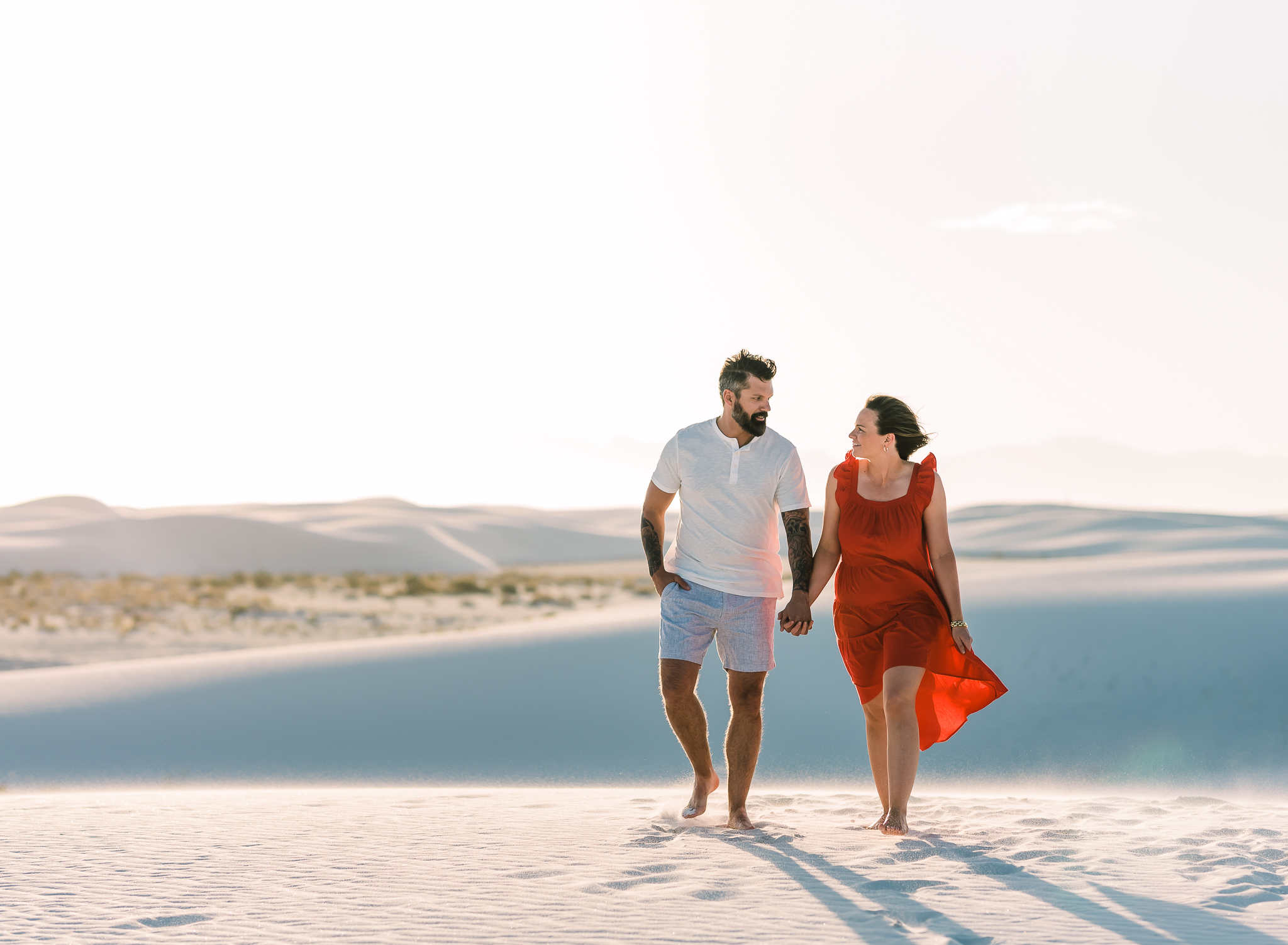 A man and woman walk hand in hand on sand dunes