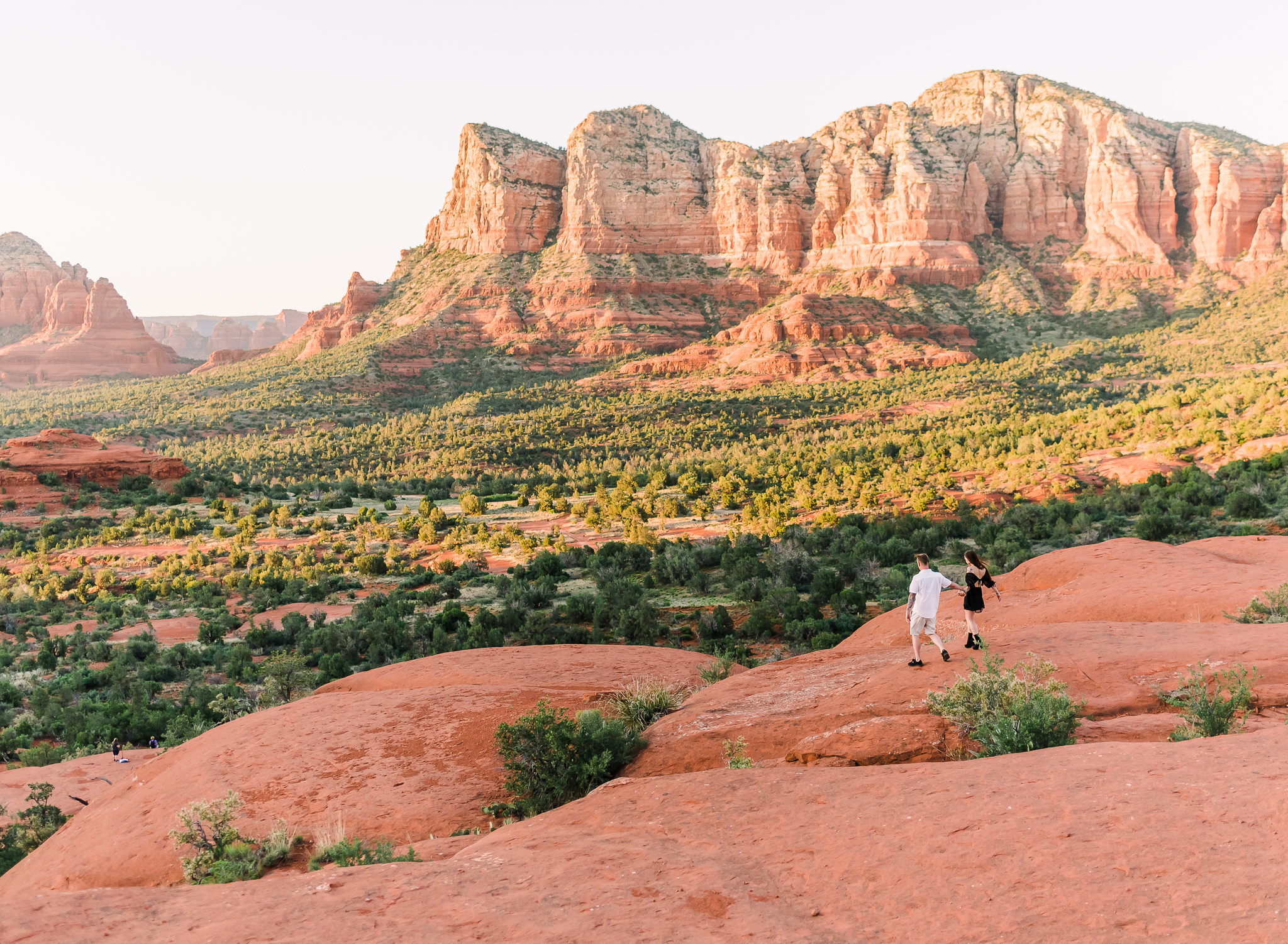 A couple walks hand in hand on the red rocks of Sedona at their couples adventure session