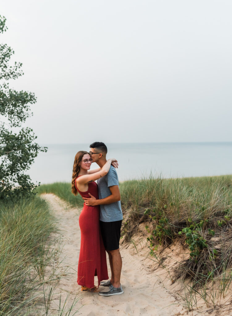 A man kisses his girlfriend on the temple  at their couples adventure session at Indiana dunes national Park