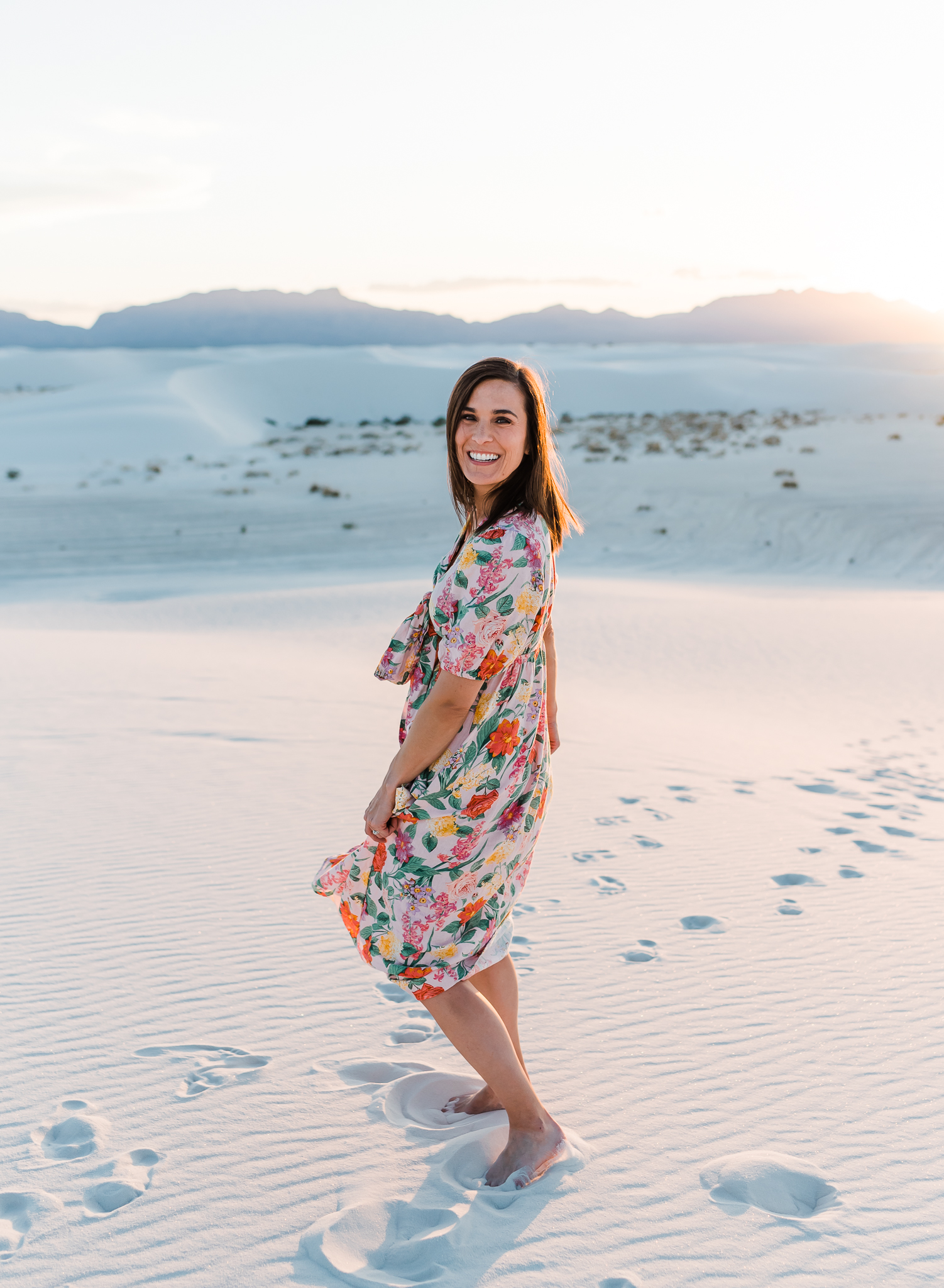 A woman swishes her dress while looking at the camera and smiling at White Sands National Park