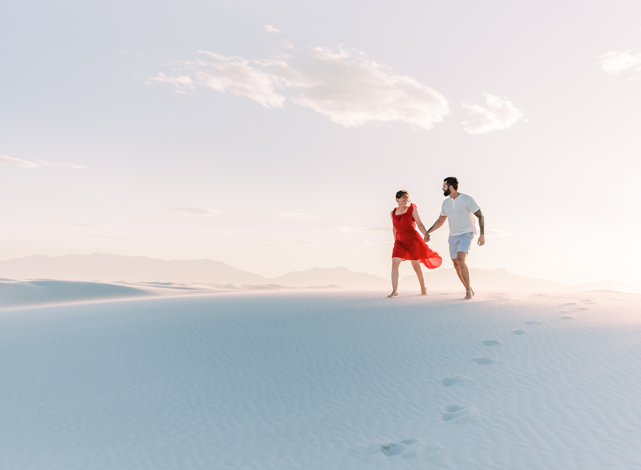 A couple runs down a giant sand dune hand in hand at White Sands National Park during their couple adventure session