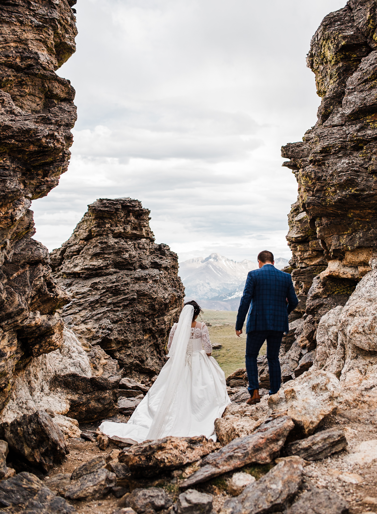 A bride and groom walk over large rocks wearing their wedding attire as they prepare to exchange vows at their colorado elopement