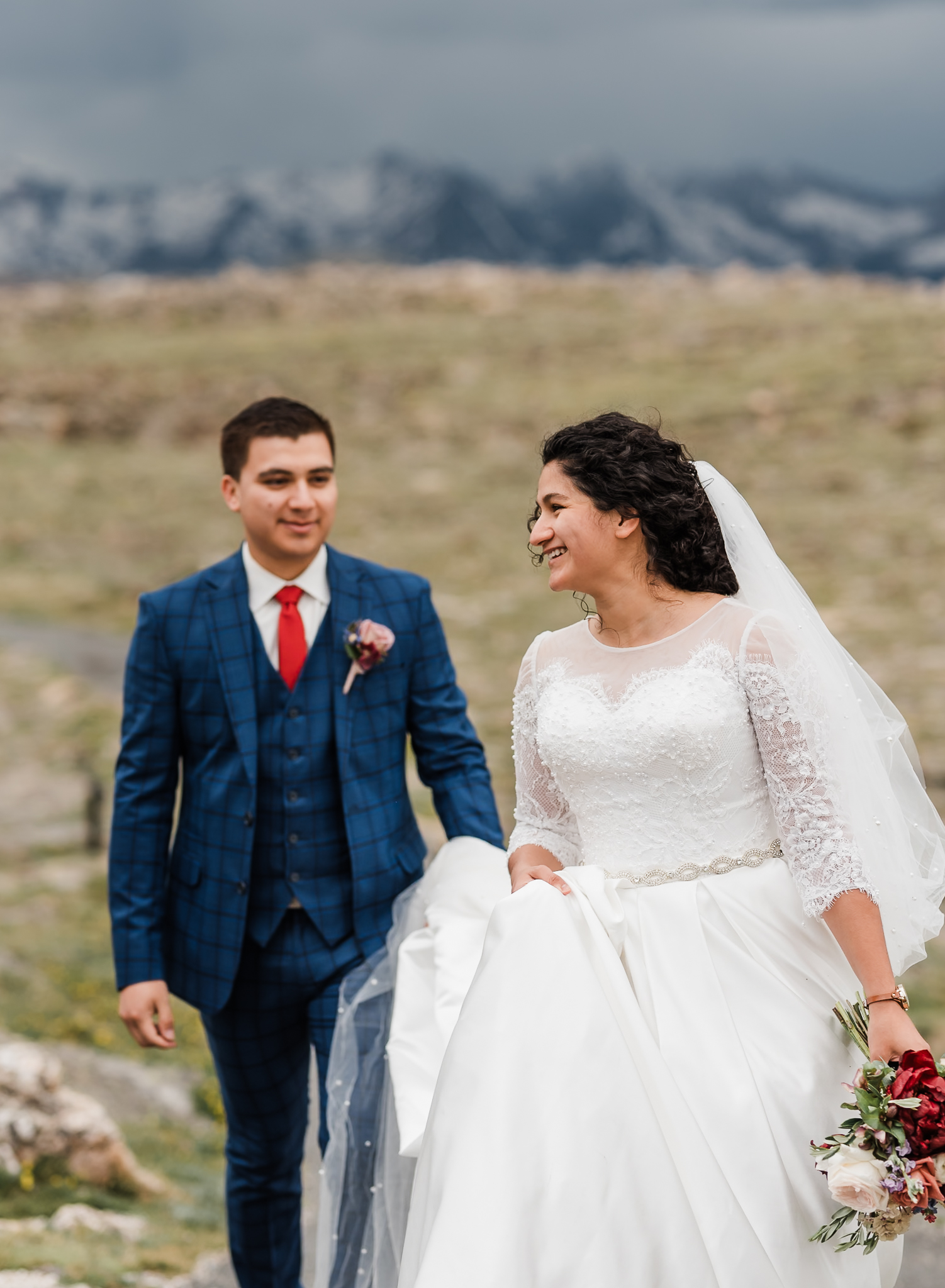 A bride and groom walk together at their Colorado elopement. The groom is slightly behind the bride helping to hold her dress up from the ground.