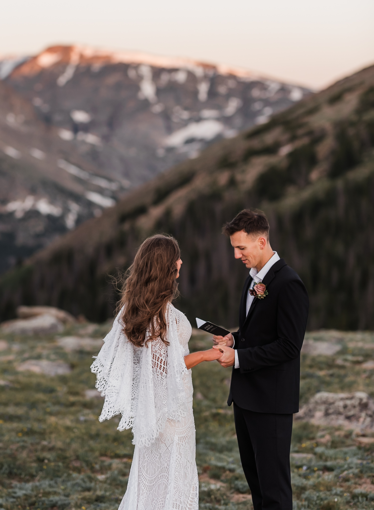 A groom is reading his vows to his bride in front of a large mountain range at Rocky Mountain National Park.