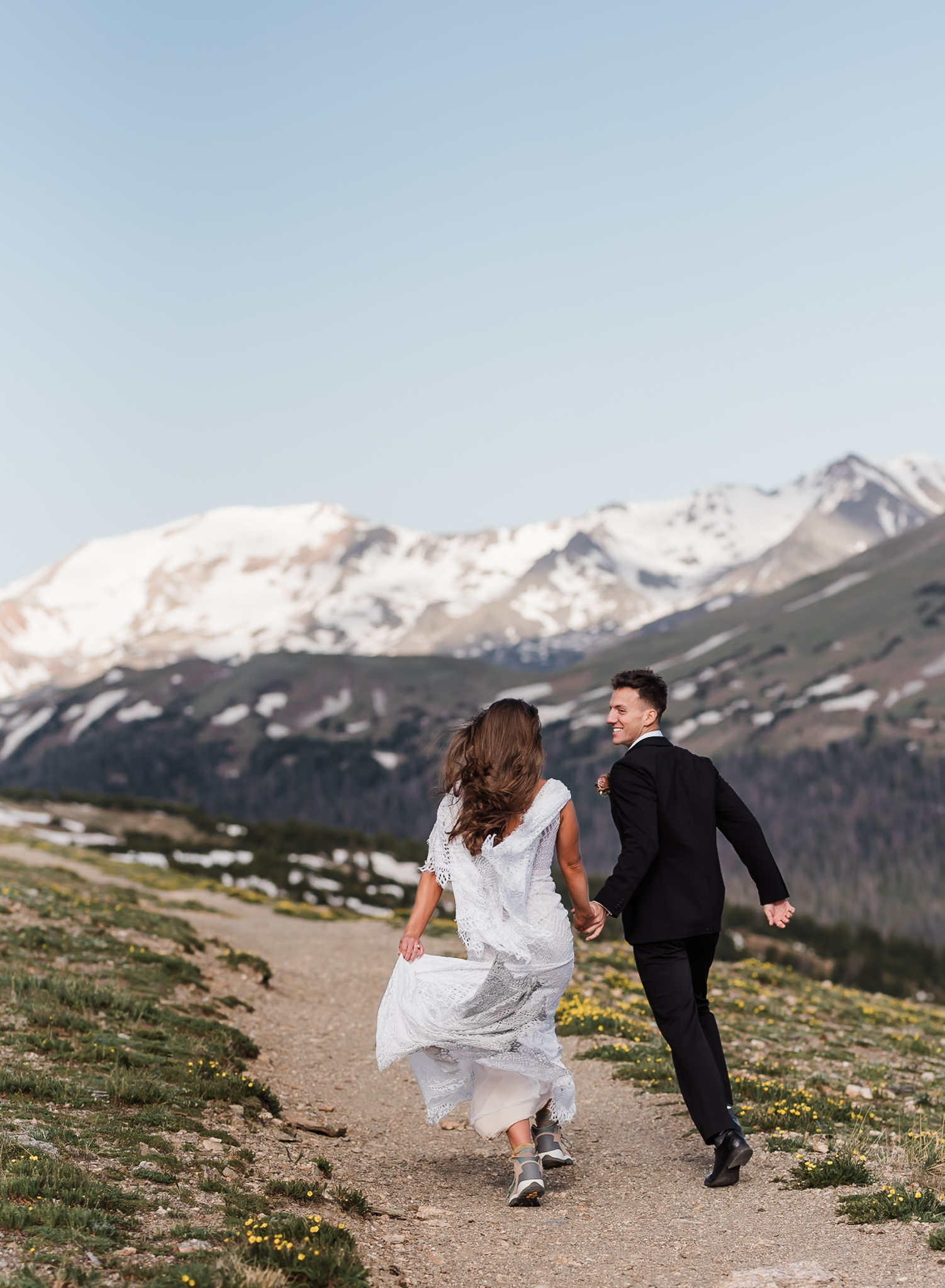 A bride and groom run hand in hand away from the camera and towards the mountains behind them at their Colorado elopement