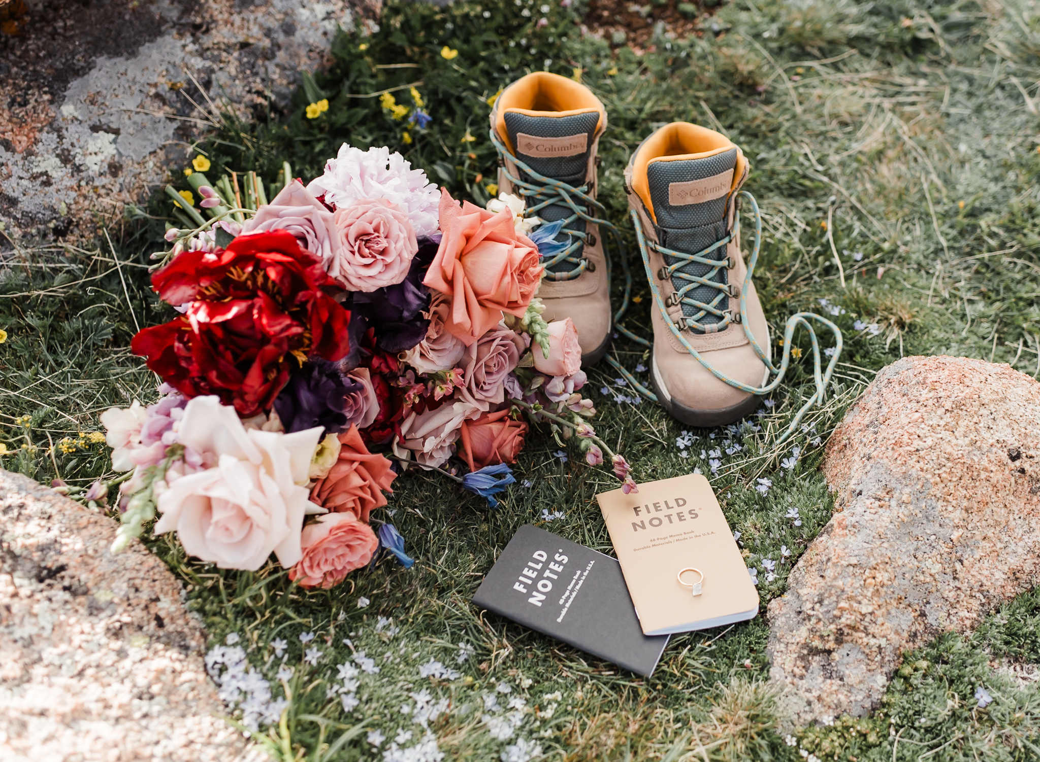 A detail shot of a mountain elopement. The shot includes hiking boots, bride and groom vow books, the bride's wedding ring, and the brides bouquet