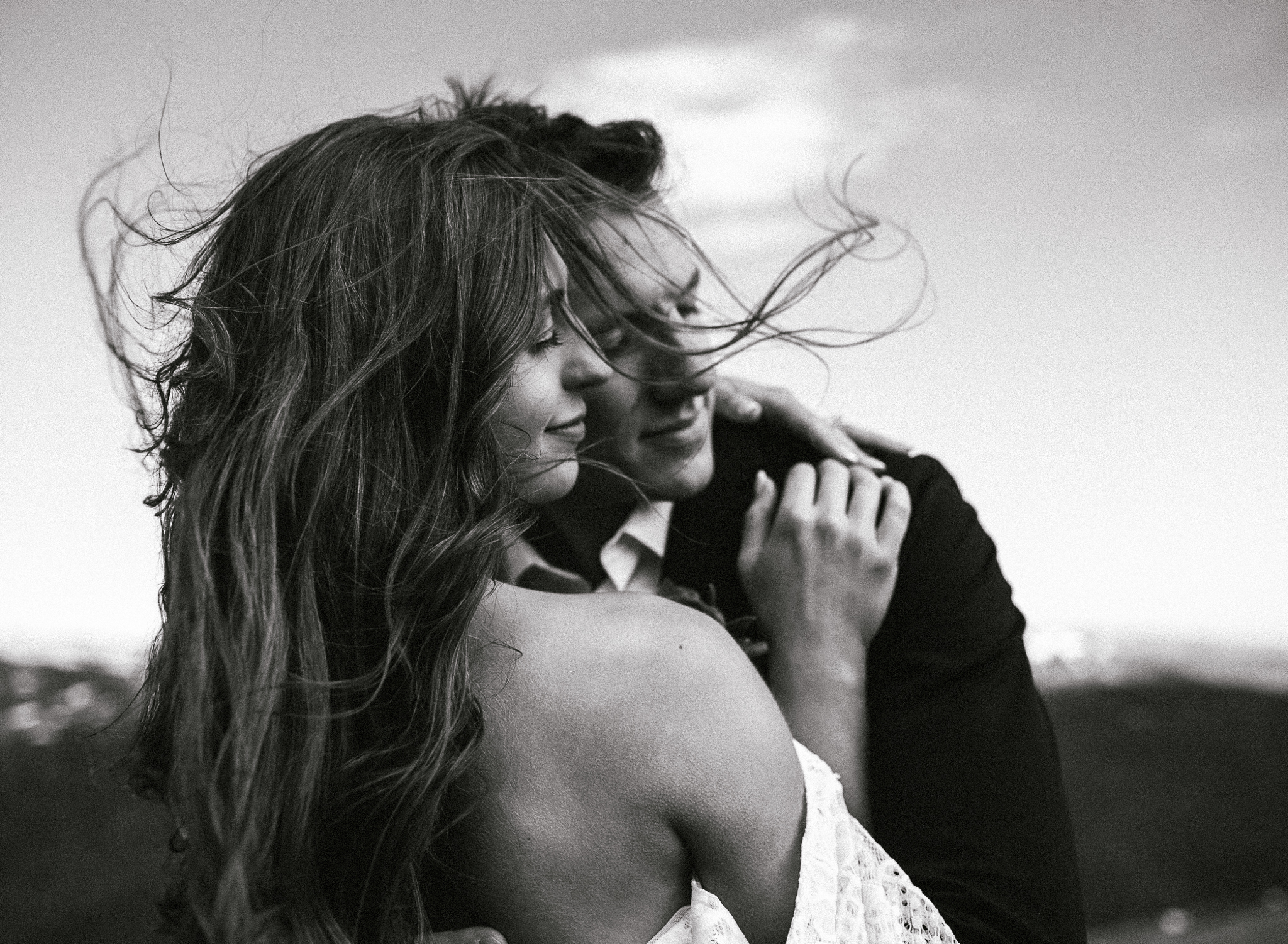 A bride and groom embrace in the mountains while the wind blows the brides hair around. This is an upclose shot of the brides hair being blown