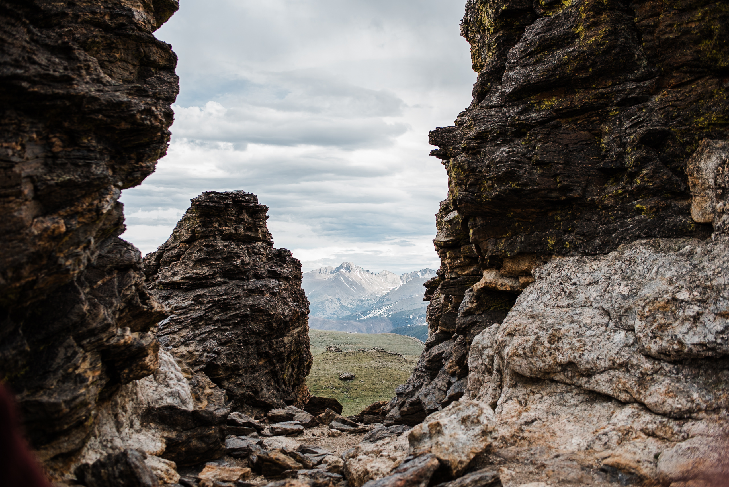 A landscape image of a large mountain range visible in the background between two large rock formations