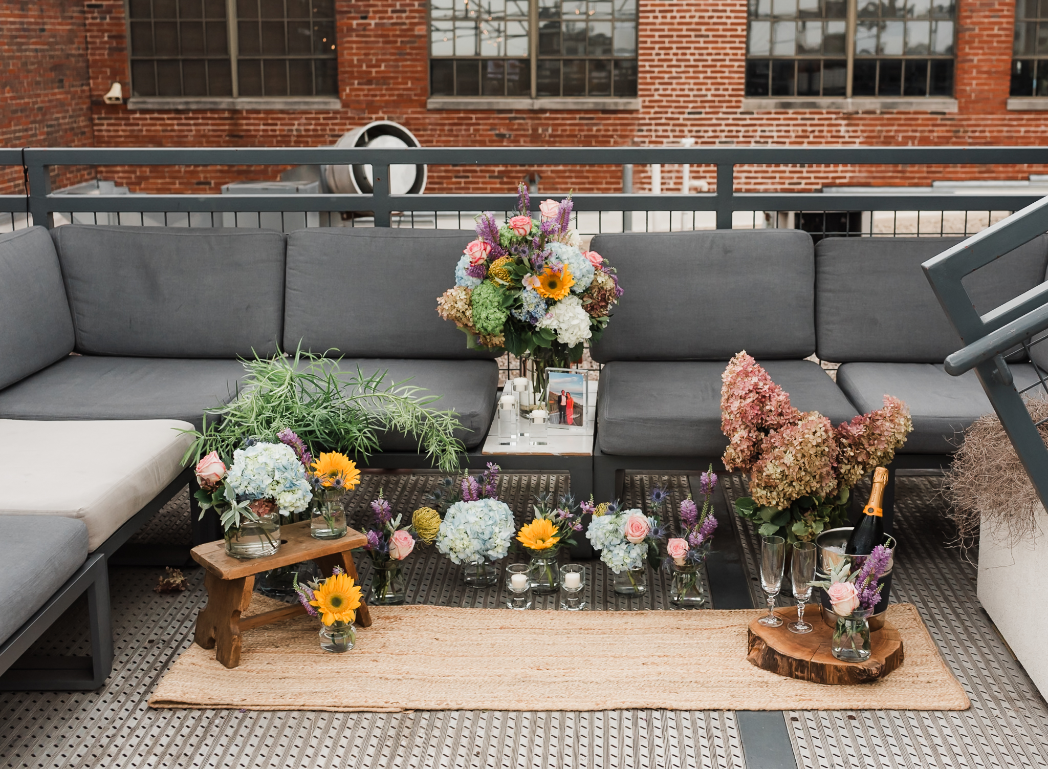 A proposal site set up filled with flowers in vases and champagne flutes, champagne and a framed photograph of the couple