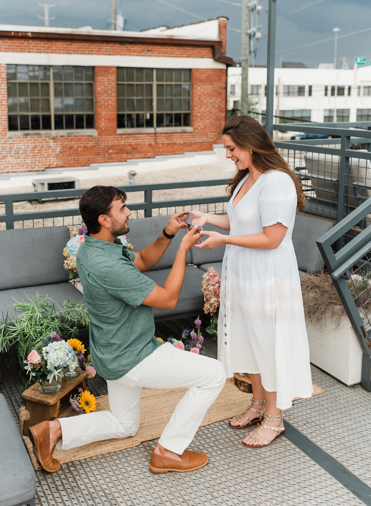 A man is down on one knee proposing to his girlfriend. She is smiling.