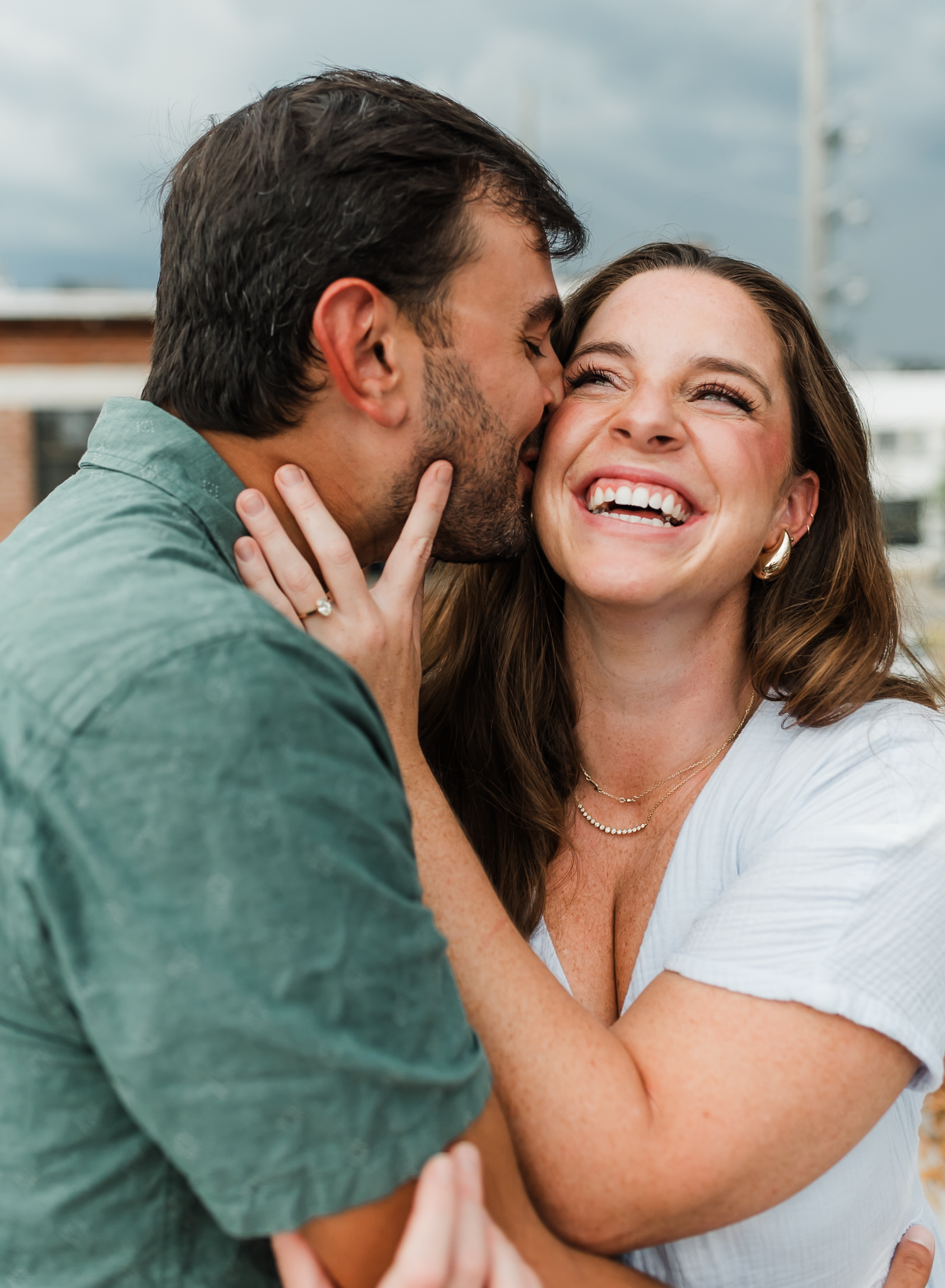 A man kisses a woman on the cheek while she laughs after just getting engaged.