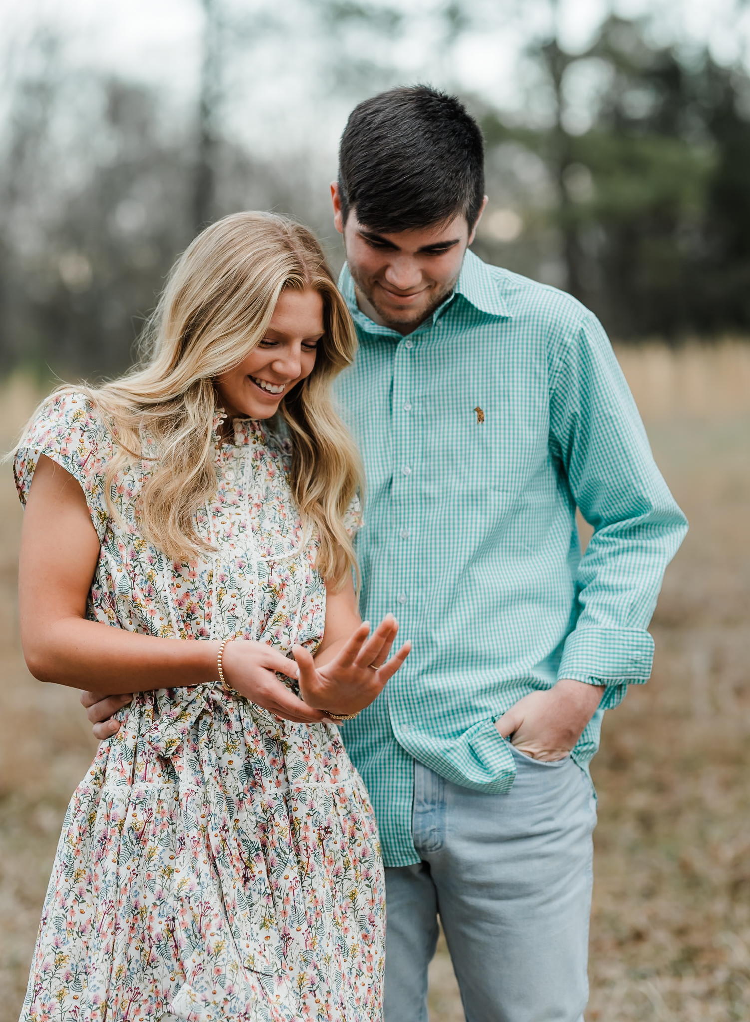 A woman is looking at her new engagement ring on her hand as her fiance looks at her hand, too