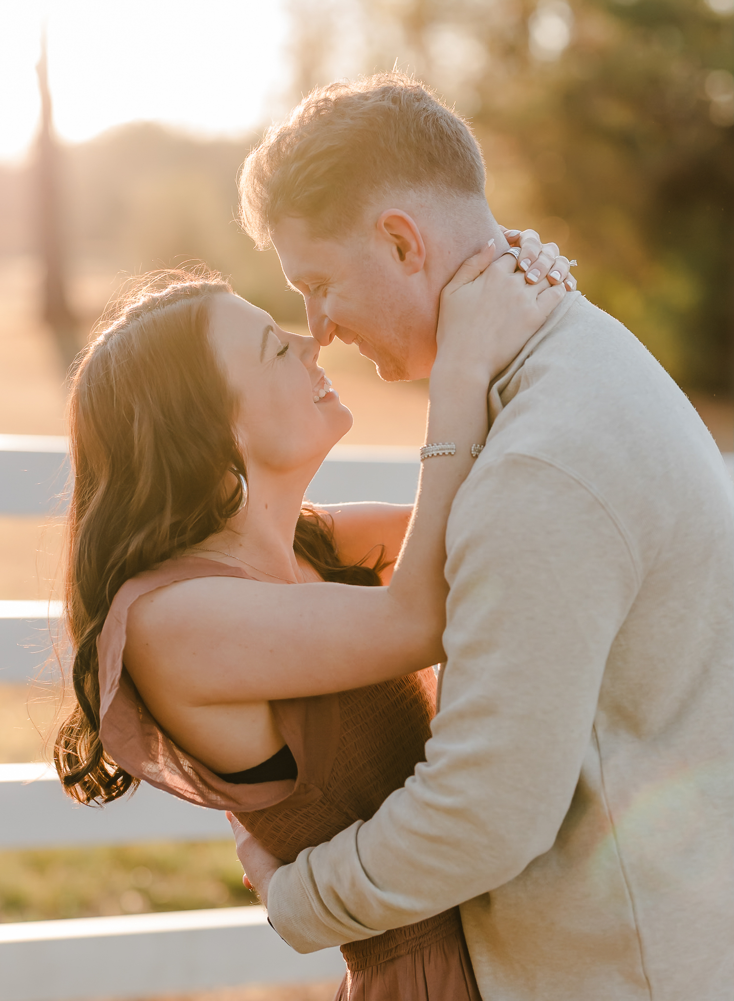 A man and woman rub noses in golden light after getting engaged.