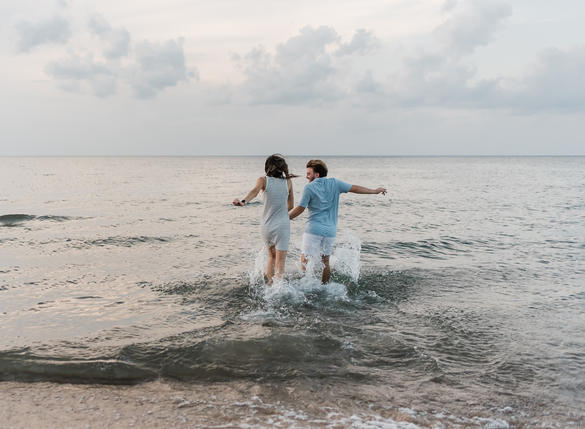 A couple runs into Lake Michigan during their adventure session at Indiana Dunes National Park on Lake Michigan