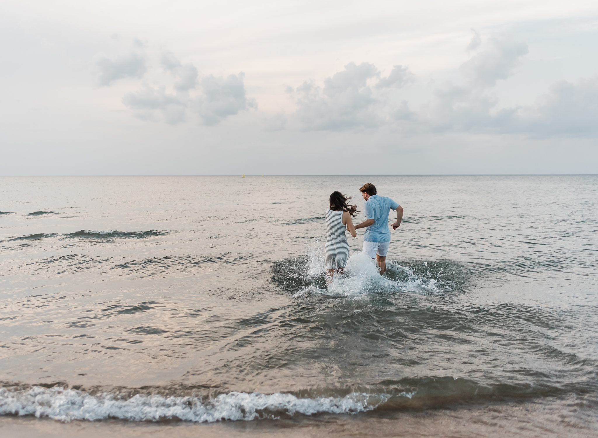 A couple walking runs into Lake Michigan
 during their adventure session at Indiana Dunes National Park on Lake Michigan