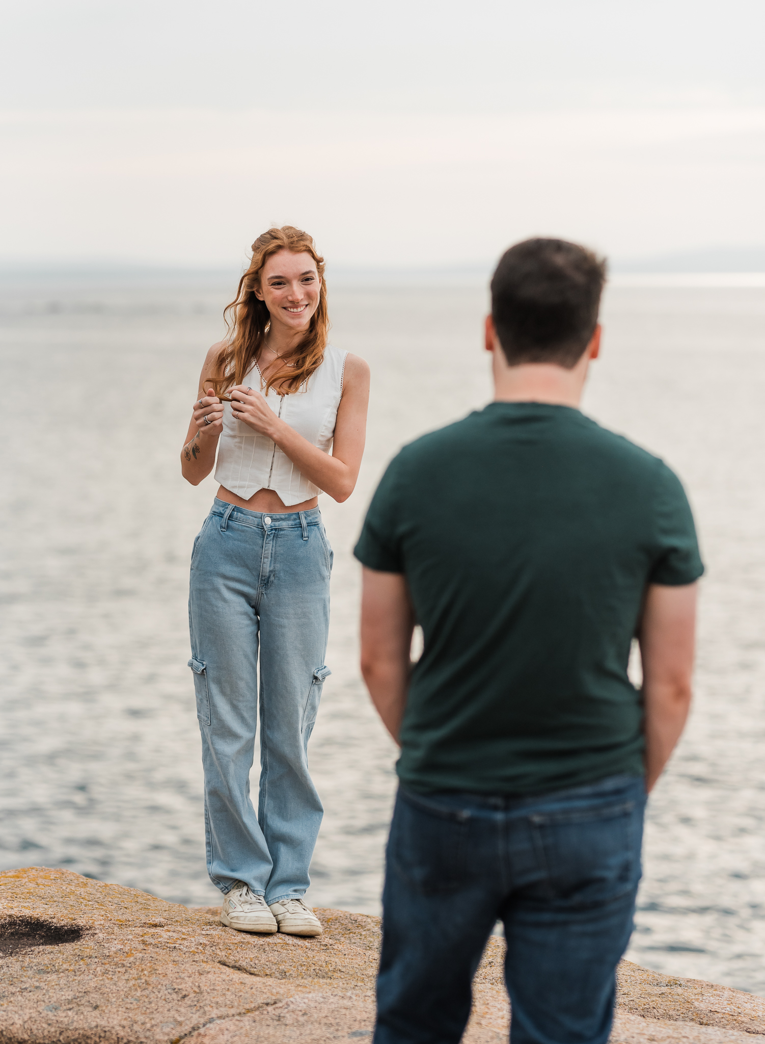 A man looks at his girlfriend as she sways back and forth on the rocky coast of Acadia National Park in Maine