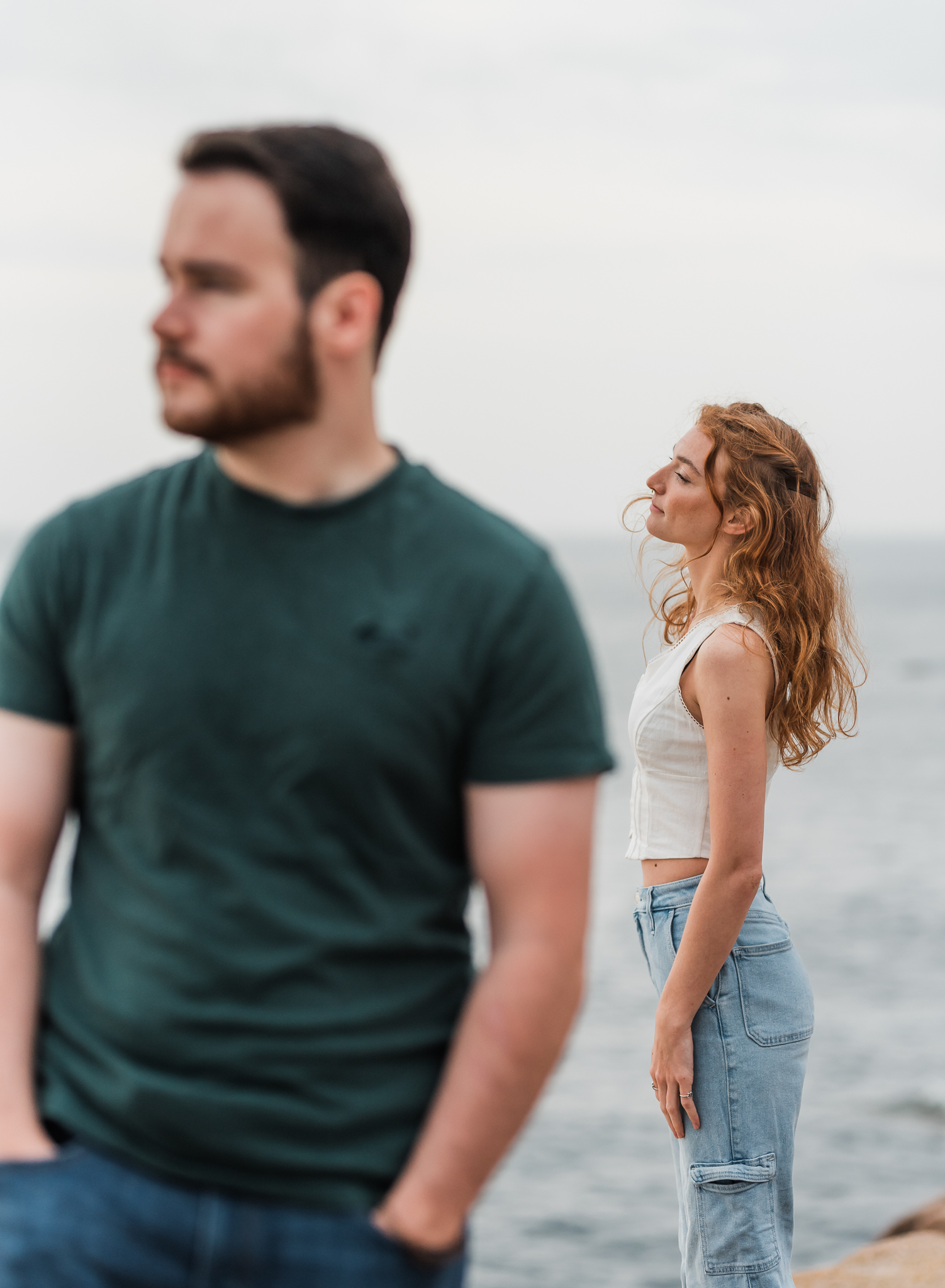 A woman lets the wind go through her hair as she looks out in the distance on the rocky coast of Acadia National Park in Maine