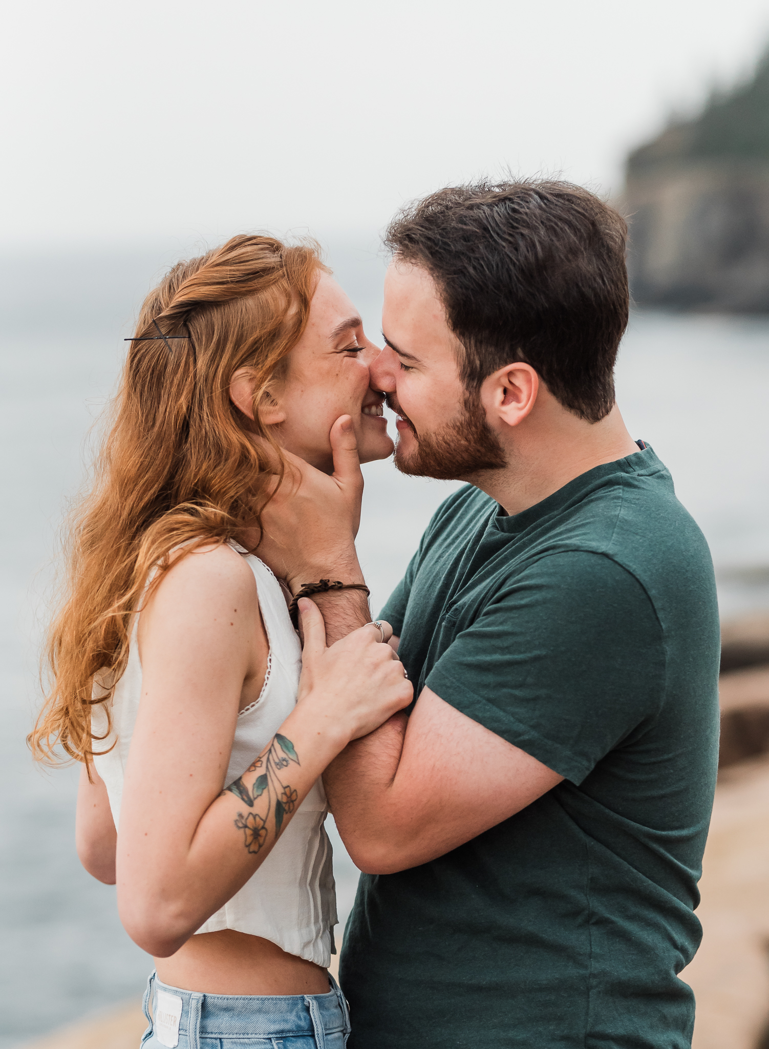 Man and woman embrace and kiss on the rocky coast of Acadia National Park in Maine