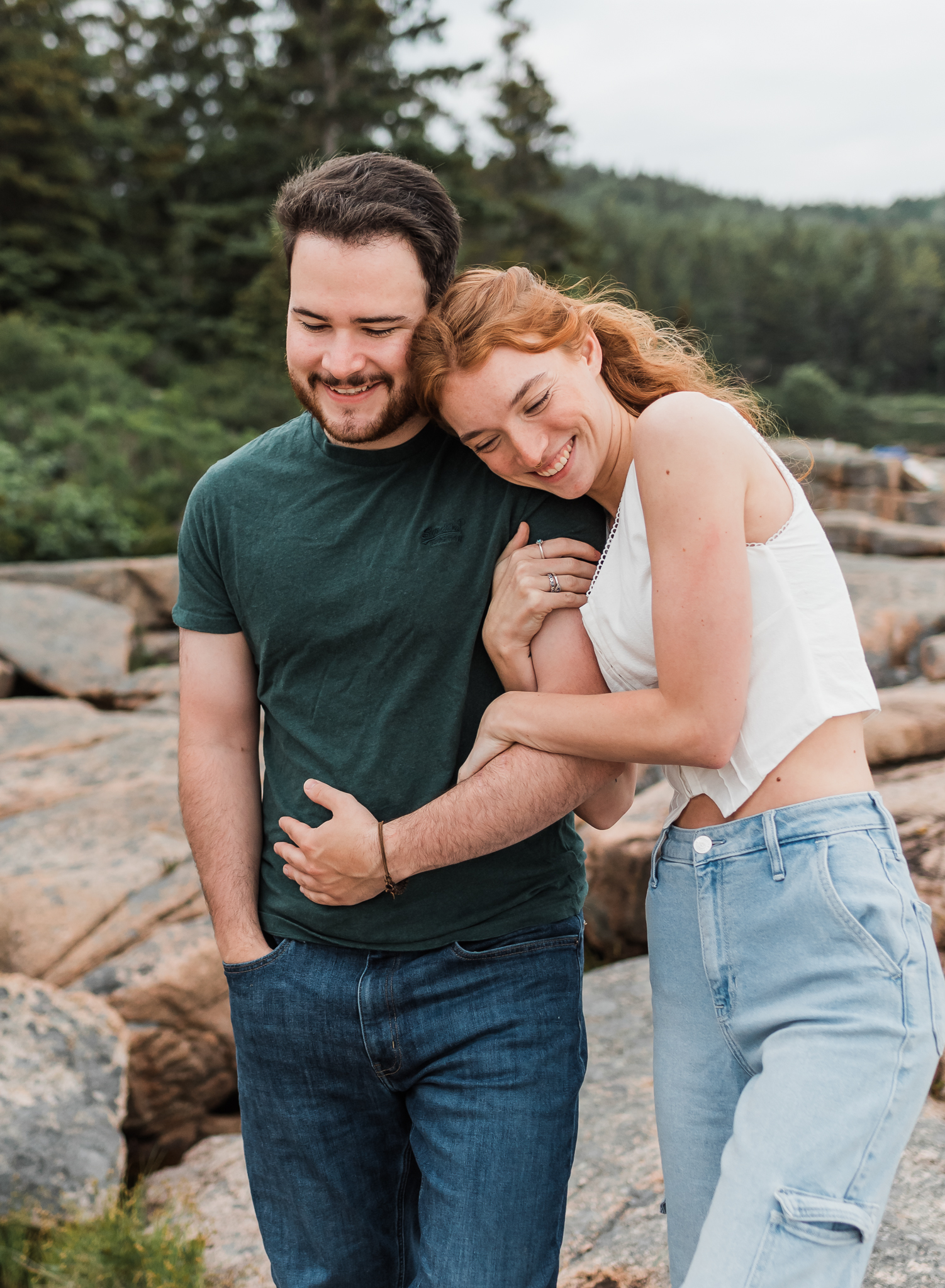 A man and woman snuggle up and walk together on the rocky coast of Acadia National Park in Maine