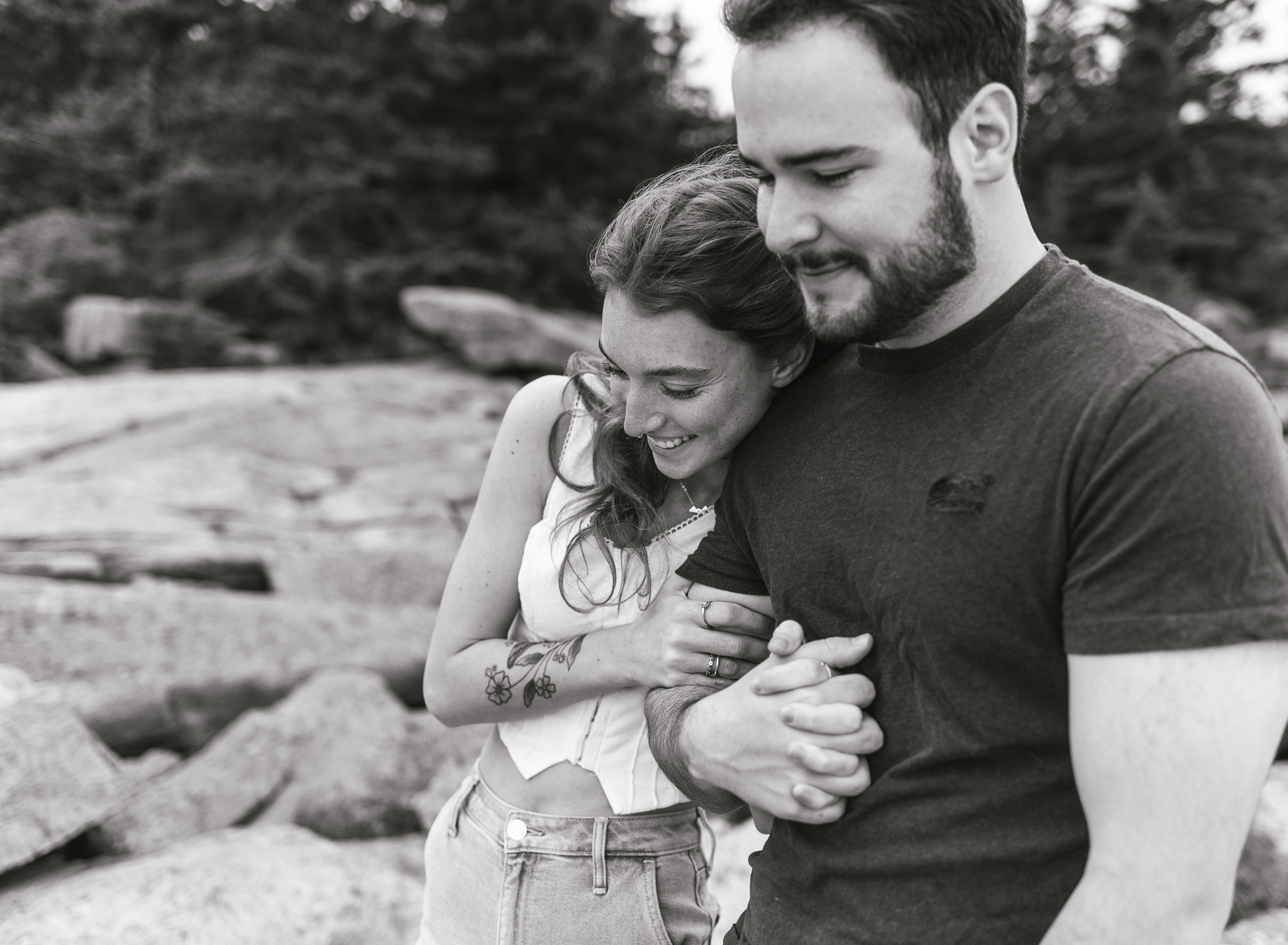 A man and woman snuggle up and walk together on the rocky coast of Acadia National Park in Maine