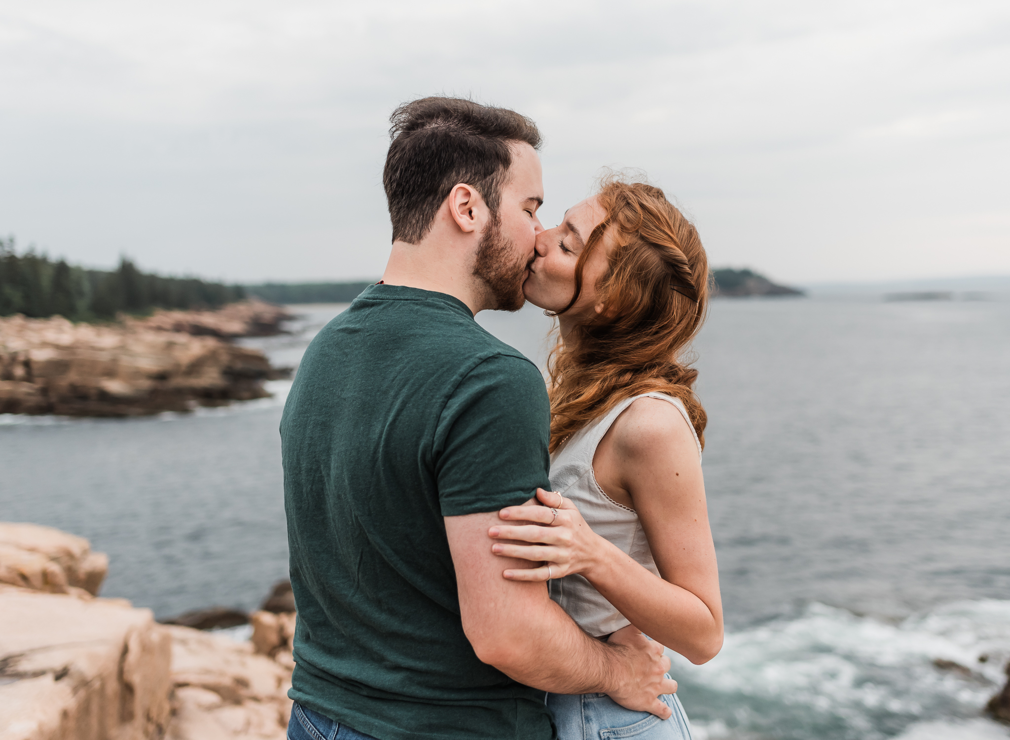 A man and woman kiss on the rocky coast of Acadia National Park in Maine