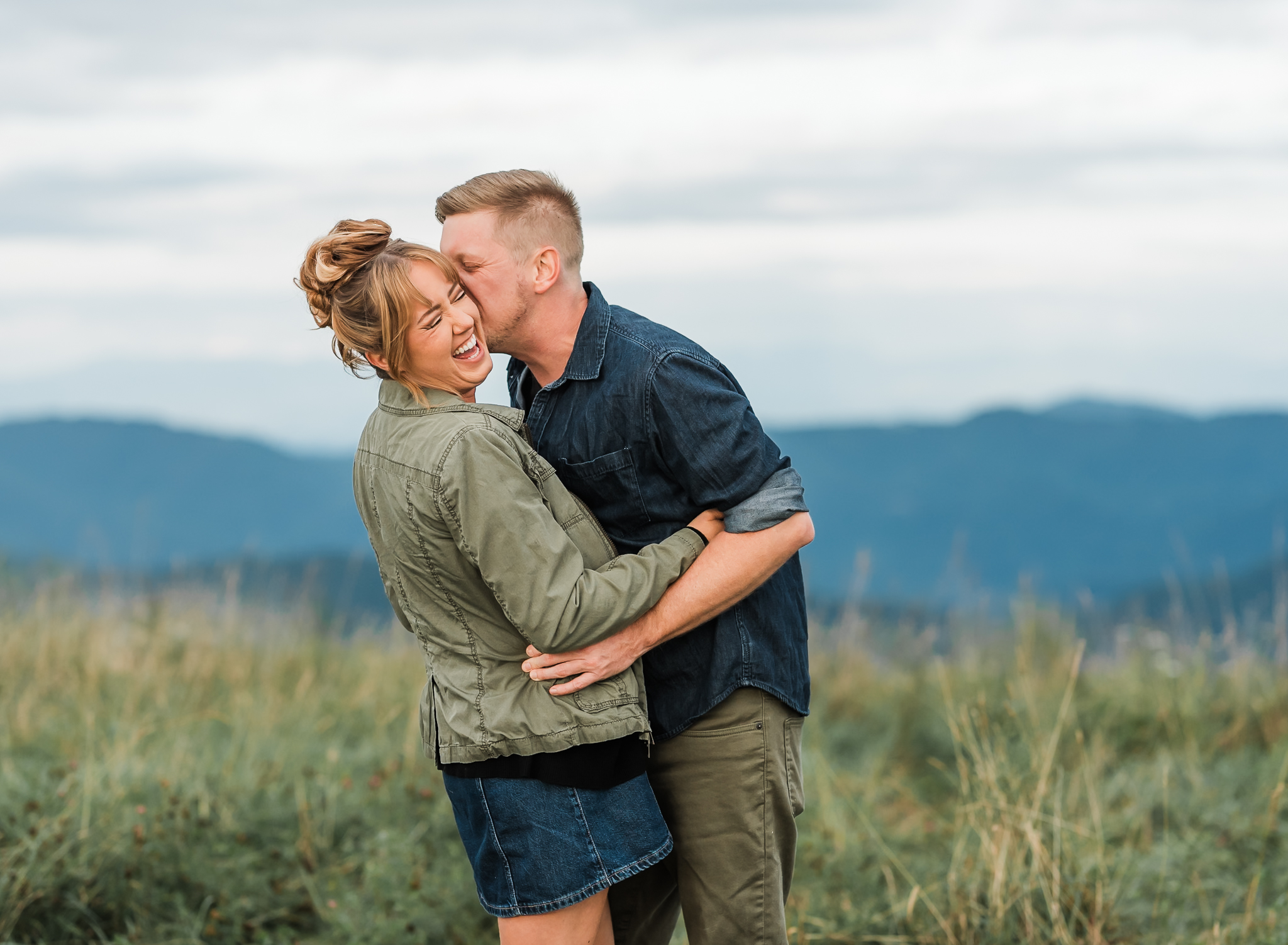 A man playfully kisses his fiance on the cheek and his fiance is laughing while at their engagement session.