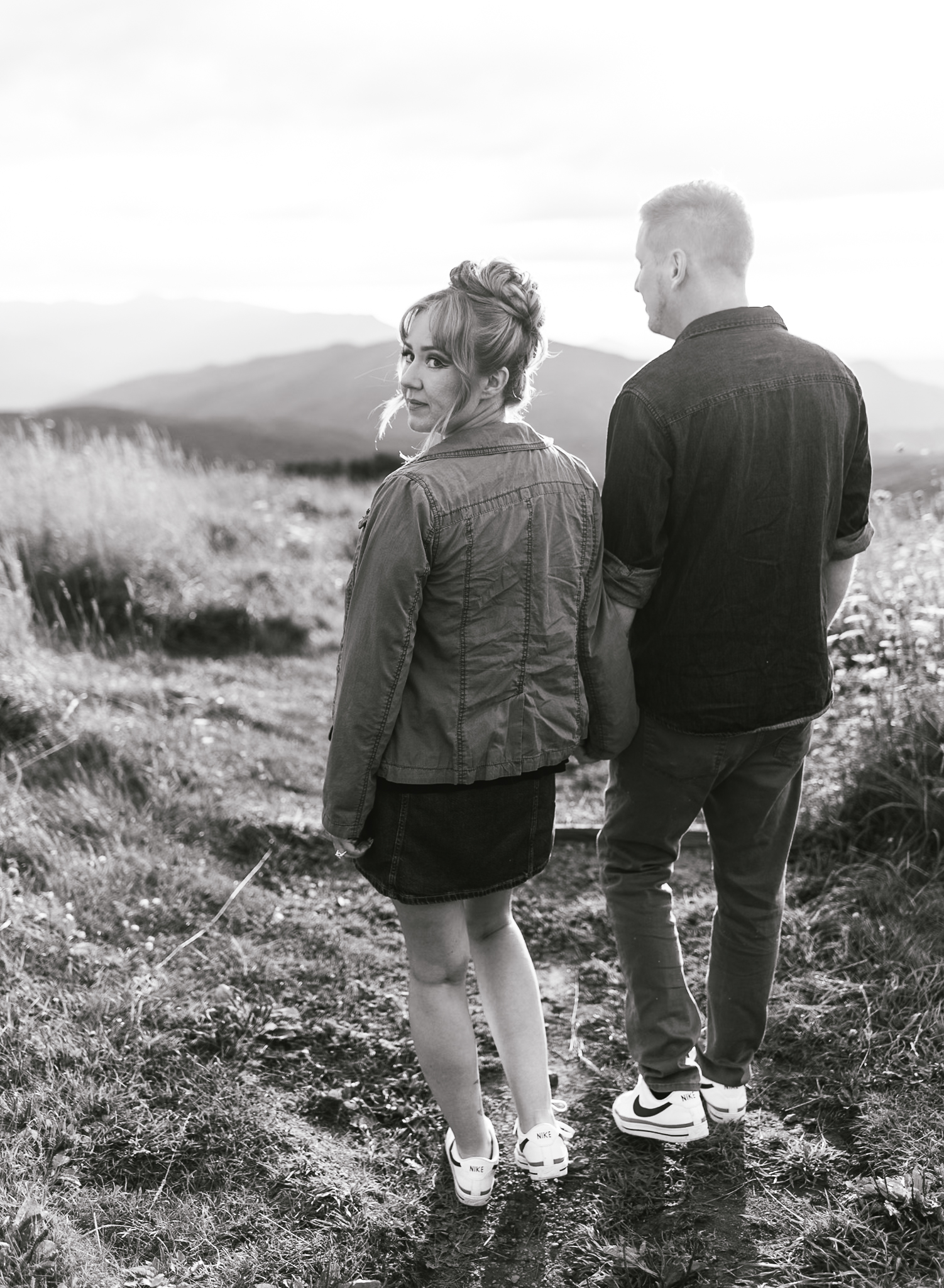 A black and white image of a couple walking together. The woman slightly turns and looks towards the camera.