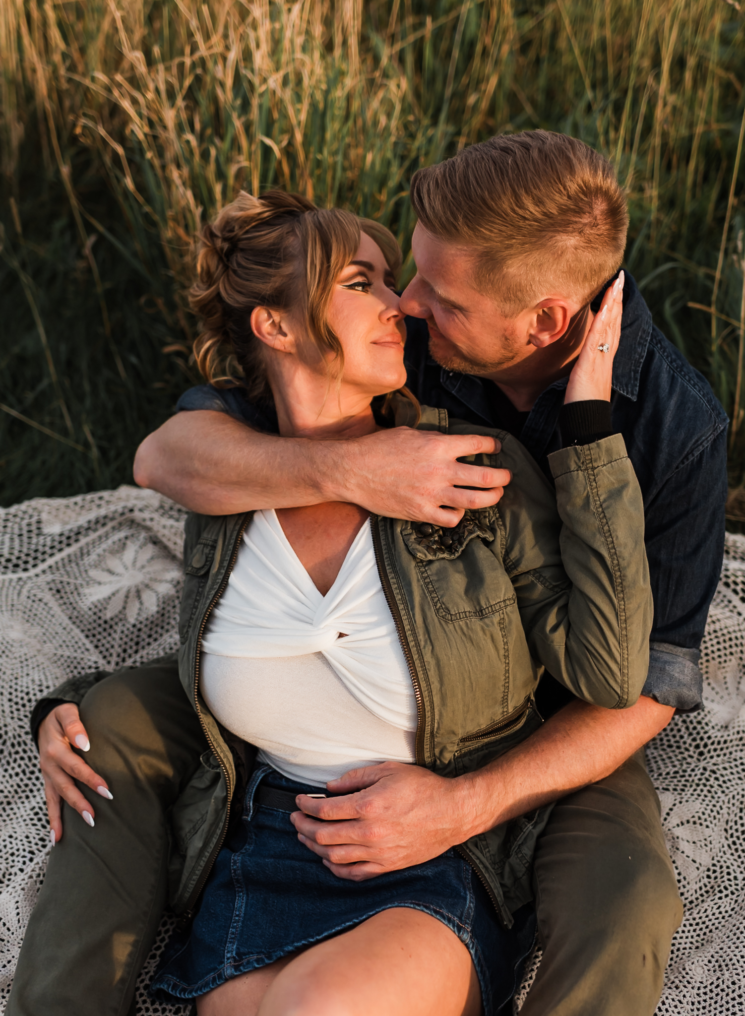 A man and woman sit together on a blanket and cuddle at their Max Patch engagement session in North Carolina