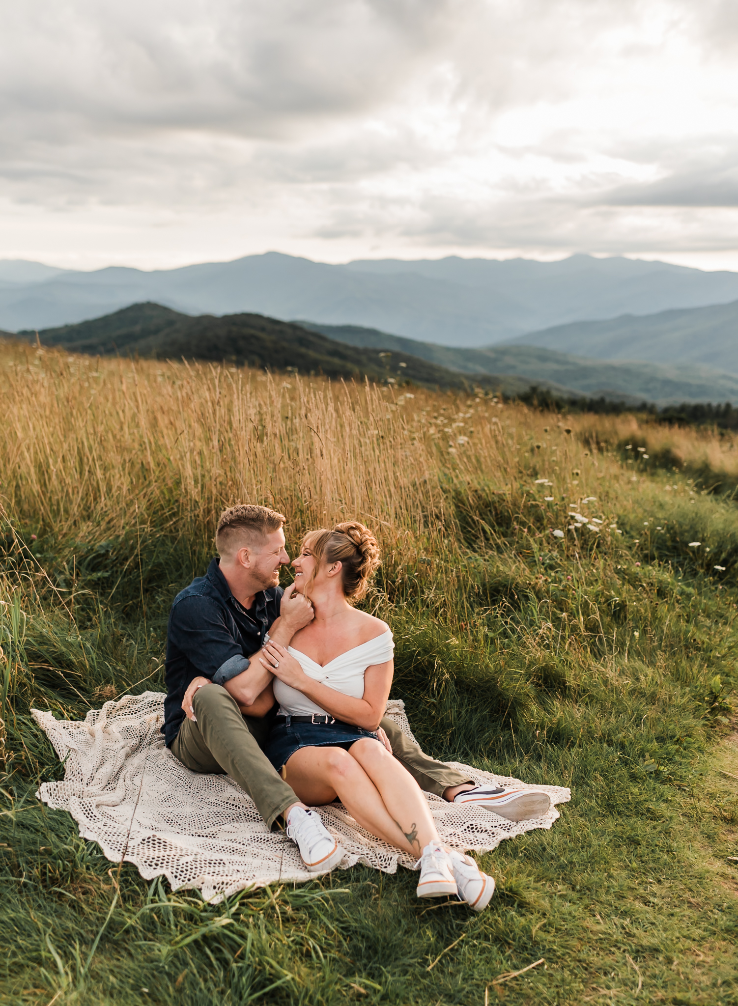 A man and woman sit together on a blanket and cuddle at their Max Patch engagement session in North Carolina