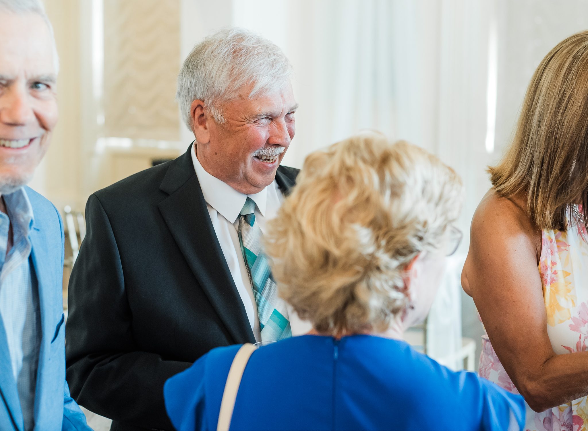 a grandad laughs while talking with guests at a wedding reception