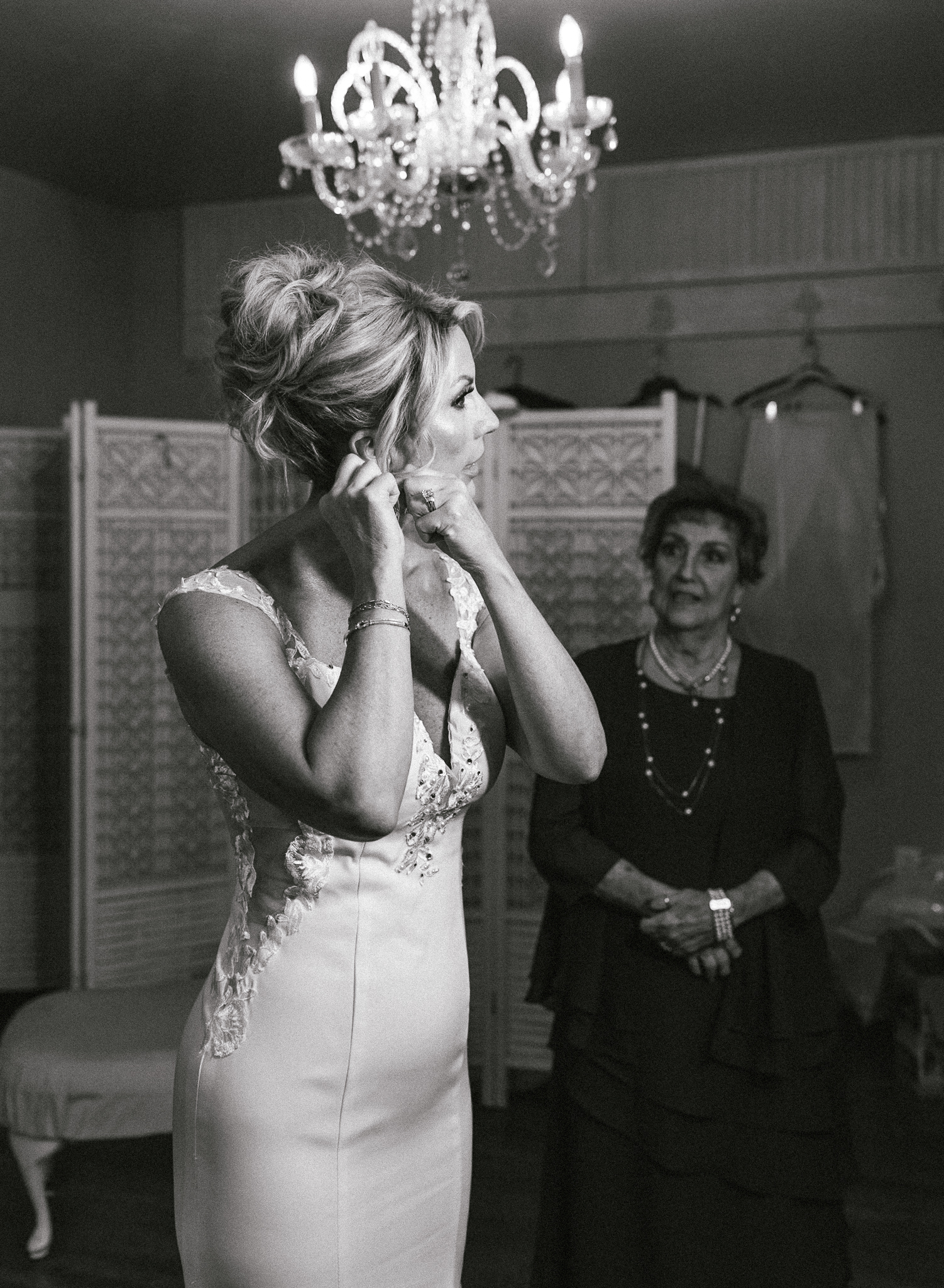 A mother watches in the background as her daughter bride puts on her earrings at her intimate wedding. 