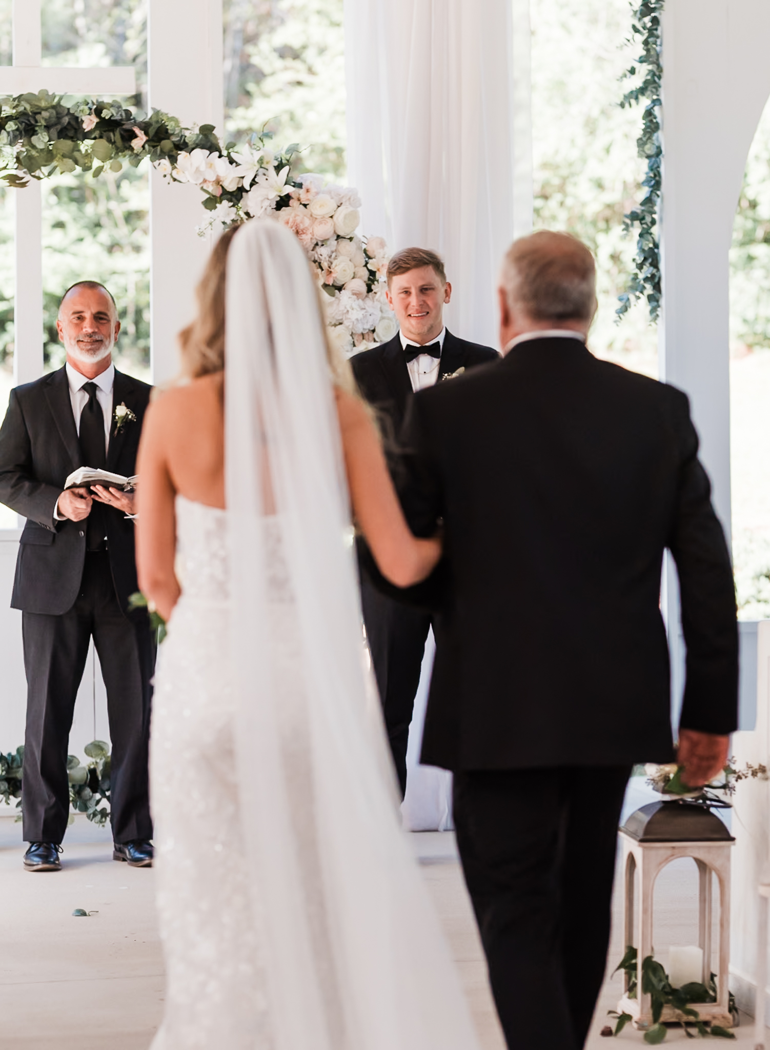 A groom smiles at his bride as she walks down the aisle with her dad