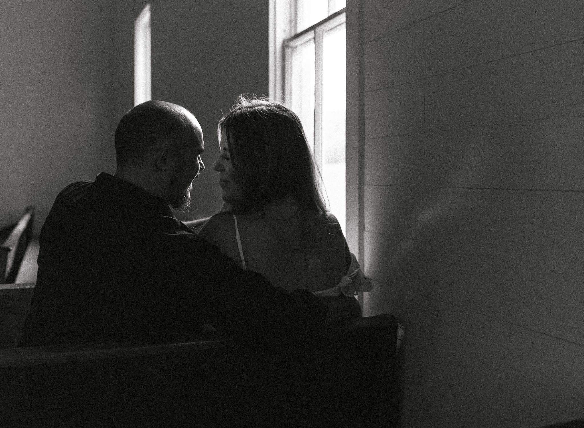 A bride and groom sit in a pew and talk and smile at each other at their intimate wedding. 