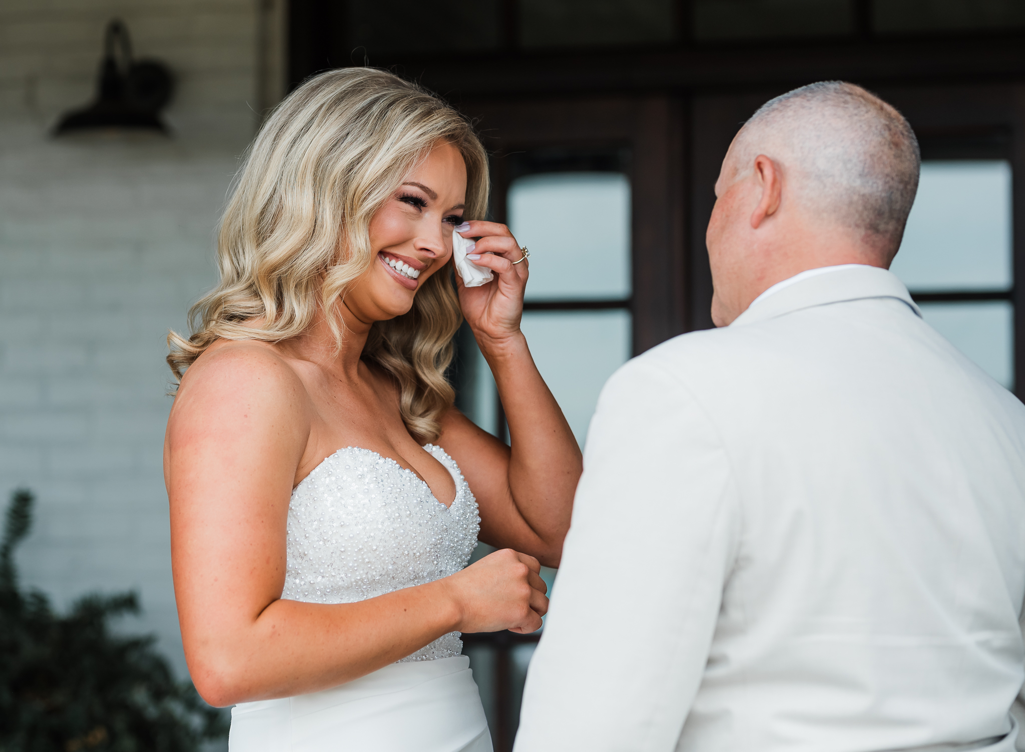 the bride is wiping away tears as she shows her dad her wedding dress for the first time at her intimate wedding .