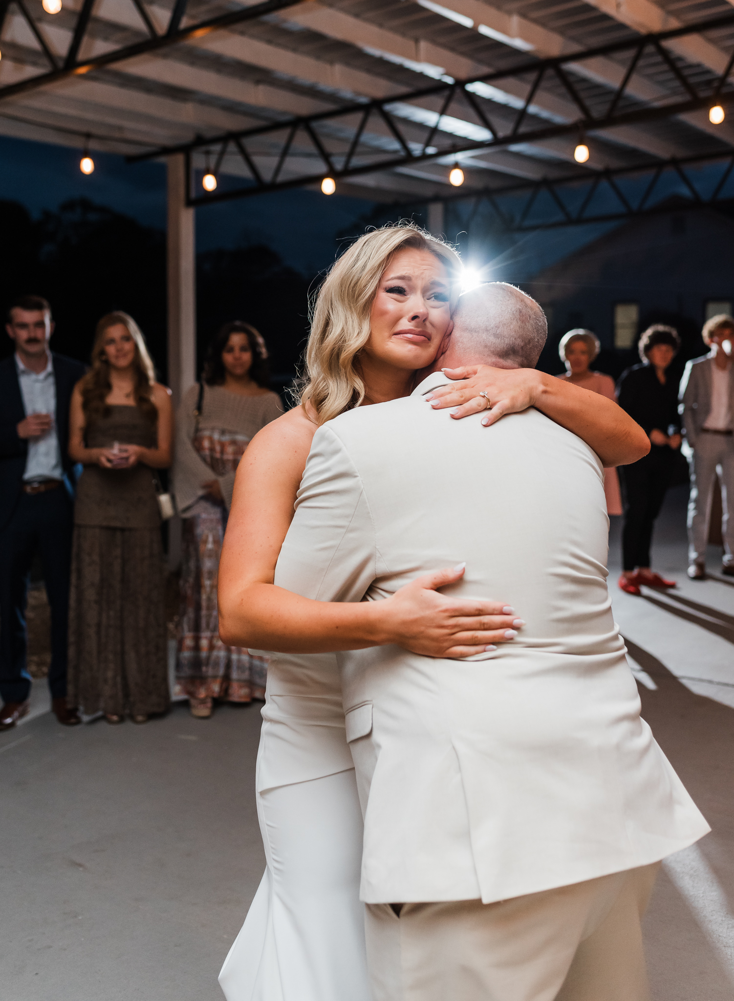 a bride and dad embrace while dancing at her intimate wedding reception. bride is crying.